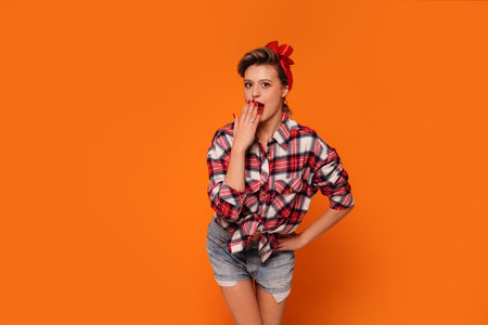 Fashion photo of happy, beautiful woman in short jeans and checkered shirt. Girl posing on orange studio background. A lot of copy space.の写真素材