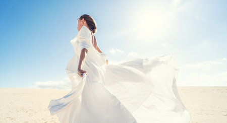 Calm woman in fashionable, maxi white wedding dress posing on the desert, dancing in sunny light. Copy space.の写真素材