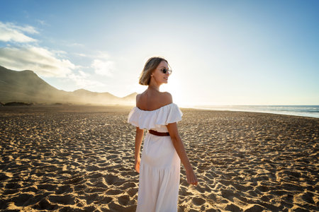 Relaxed woman enjoying sun on a beautiful sandy beach at sunset. Summer vacation, freedom, happiness concept. A lot of copy space.の写真素材