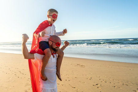 Happy family concept. Father and son playing superhero on the beautiful sunset beach , having fun together outdoors, wearing red masks and capes. summer holiday. copy space.の写真素材