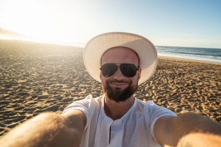 Happy, smiling man on vacation at the beach, taking selfie. Handsome guy in white summer hat and black sunglases.の写真素材