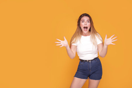 Excited, shocked young woman keep mouth open, screaming. Yellow studio background. Copy space. Student. Real people emotions.の写真素材