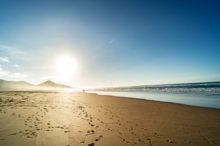 Sunrise on the coast with a couple walking on the beach. Landscape. Fuerteventura, Canary Island, Spain.の写真素材