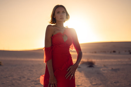 Romantic woman in a long red dress posing at a golden sunset light on the desert. A lot of copy space.の写真素材