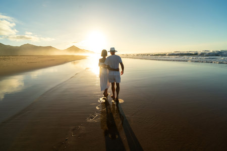 Back view of romantic couple walks along a sandy beach on the Fuerteventura island. Couple in love at sunset by the sea on vacation. honeymoon trip.の写真素材