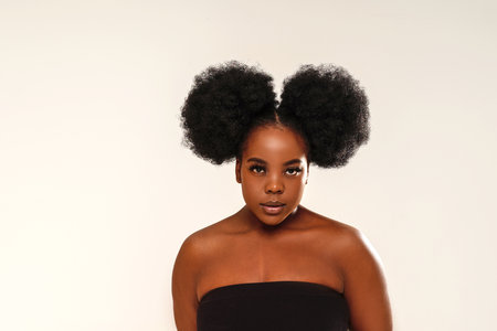 Beauty portrait of cute woman with afro hair looking at the camera, posing over studio background. Girl with long lashes and delicate makeup. A lot of copy space.の写真素材