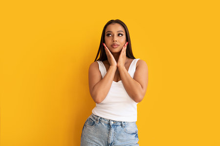 Portrait of a delicate young woman posing isolated over yellow studio background. Emotional female model looking aside at free space. Sale And Discount Concept.の写真素材