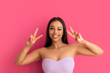 Happy woman smiling, looking at the camera, posing on a pastel pink Studio Background. Real people emotions, toothy smile. Fashionable young girl, A lot of copy space.の写真素材