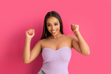 Joyful woman smiling, looking at the camera, posing on a pastel pink Studio Background. Real people emotions, toothy smile. Fashionable young girl, A lot of copy space.の写真素材