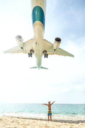 Photo of airplane flies extremely low over the sandy beach and one tourist kid. Travel and tourism concept. Thailand.の写真素材