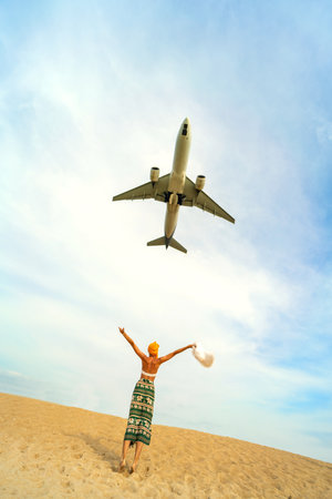 Photo of airplane flies extremely low over the sandy beach and one tourist woman. Travel and tourism concept. Thailand.の写真素材