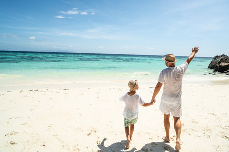 Father and son holding hands, having fun together, walking on the tropical beach. Fathers day. Summer vacation. Copy spaceの写真素材