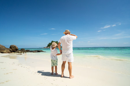 Father and son holding hands, having fun together, walking on the tropical beach. Fathers day. Summer vacation. Copy spaceの写真素材