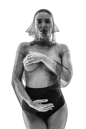 Fashionable pregnant woman posing in studio, looking at the camera and holding her belly. Girl wearing stylish net dress. A lot of copy space.の写真素材