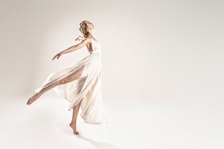 Ballerina in maxi dress dancing over light studio background. Ballet Dancer. Modern Dance. Graceful Woman. Hobby. Full length photo. A lot of copy space.の写真素材
