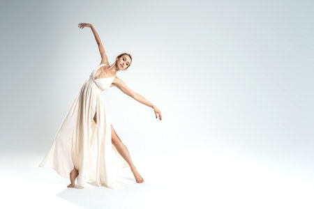 Ballerina in maxi dress dancing over light studio background. Ballet Dancer. Modern Dance. Graceful Woman. Hobby. Full length photo. A lot of copy space.の写真素材