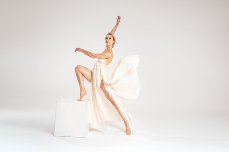 Young female blonde dancer wearing elegant dress dancing over grey light studio background. Copy space. Ballerina. Hobby.の写真素材