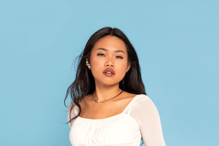 Asian Beauty Woman with long dark hair wearing jewelry, looking at camera. Girl posing on blue pastel studio background.の写真素材