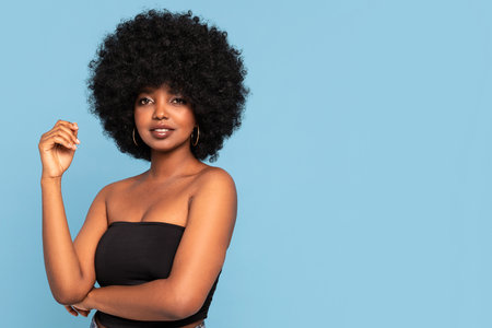 Portrait of attractive young African American female model in black top, with afro hairstyle, looking to the camera. A lot of copy space. Blue pastel studio background.の写真素材
