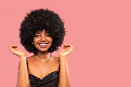 Fashion studio portrait of beautiful smiling woman with afro curls hairstyle. Beauty face of cheerful girl. Real people emotions. A lot of copy space on the pink pastel studio background.の写真素材