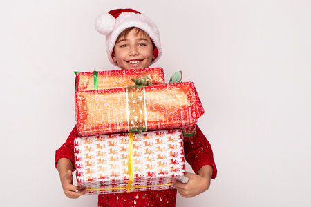 Happy boy in a red Santa hat holding boxes of Christmas gifts, smiling to the camera.の写真素材