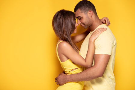 Sexy beauty couple hugging and almost kissing. Two beautiful people in love, spending time together. A lot of copy space on yellow studio background.の写真素材