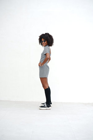 Young woman with afro hairstyle standing and posing on the white wall. Girl wearing fashionable casual clothes, street style. A lot of copy space.の写真素材