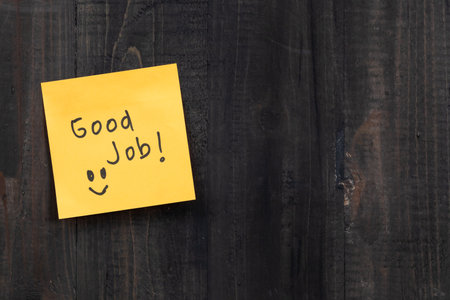 Good job written on a yellow sticky note on a wooden background.の写真素材