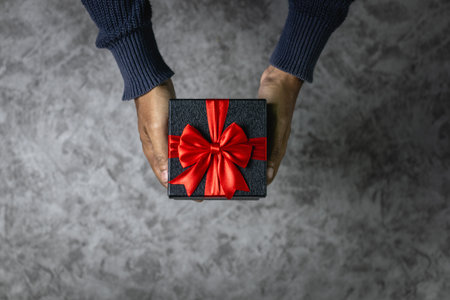 Man's hands holding a gift box with a red bow on a gray background.の写真素材