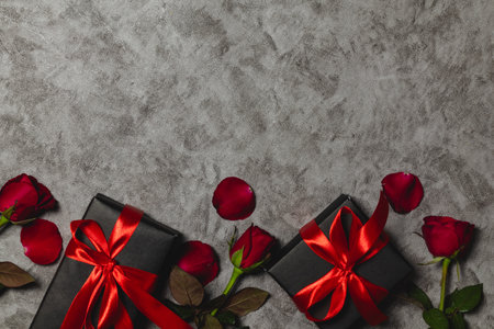 Black gift box with red ribbon and rose flowers on grey background. Top view with copy spaceの写真素材