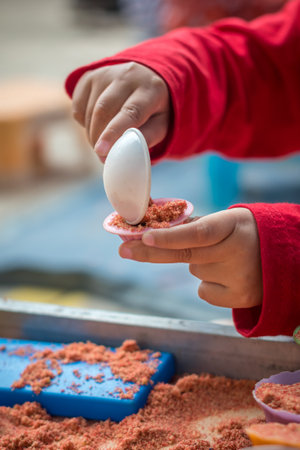 Close up of a child's hand holding a spoon and playing with colored sandの写真素材