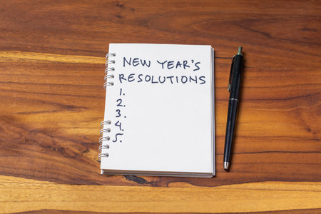 New year resolutions written on notebook with pen on wood table background.