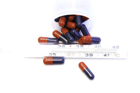 Pills in capsules with thermometer at white blank  