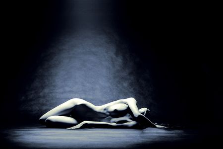 Studio shot of nude model laying in pool of lightの写真素材