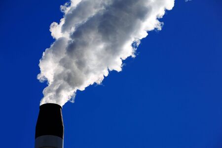 Smoke stack spewing smoke out of it with blue sky in background