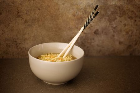 A bowl of Asian noodles on bench with chopsticks
