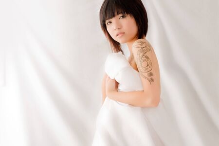 Asian beauty clutches sheets to her naked body on white backgroundの写真素材