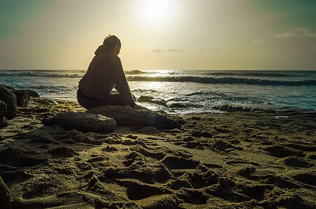 Man sitting on rocks in the light of sunset at seaの写真素材