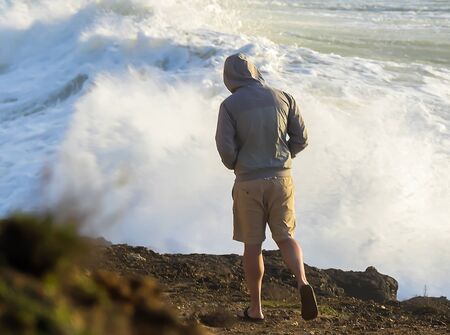 Man in gray jacket with hood on head on cliff
