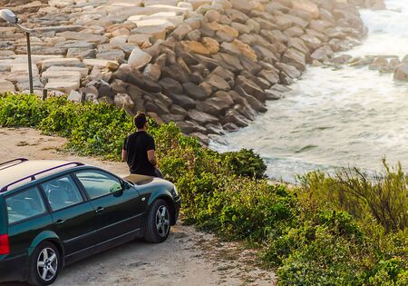 Man in black shirt admiring the ocean on the hood of the carの写真素材