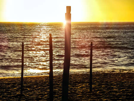 Sunset on a beach with wooden poles in the foreground in yellow and brown lightsの写真素材
