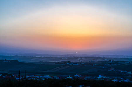 Morning landscape at sunrise with a few hills with houses and an orange blue sky
