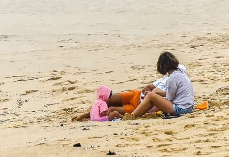 A young family at the beach on the sand with a small child on a cloudy dayの写真素材