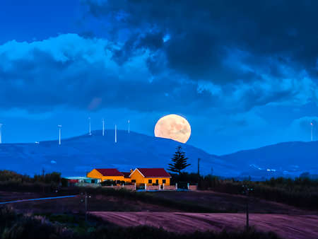 Landscape with full moon sunrise coming out of the hills in the eveningの写真素材