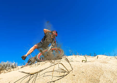 Cyclist skidding off a sand dune with one foot raised against a blue skyの写真素材