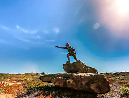 Landscape with a man on a rock with his arm outstretched against a background of blue skyの写真素材