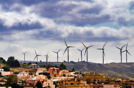 Field with windmills on a hill near the city with a cloudy sky with dramatic clouds