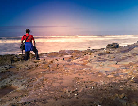 Man in a T-shirt blushes the edge of the ocean in the evening light