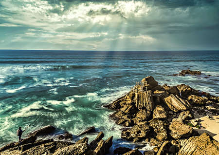 Seascape with rocks in the sea and cloudy sky with sunbeams