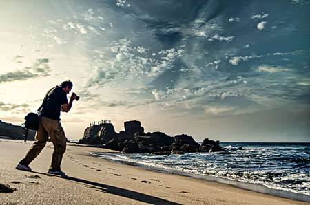 A man photographing on the beach in the evening light with a dramatic skyの写真素材